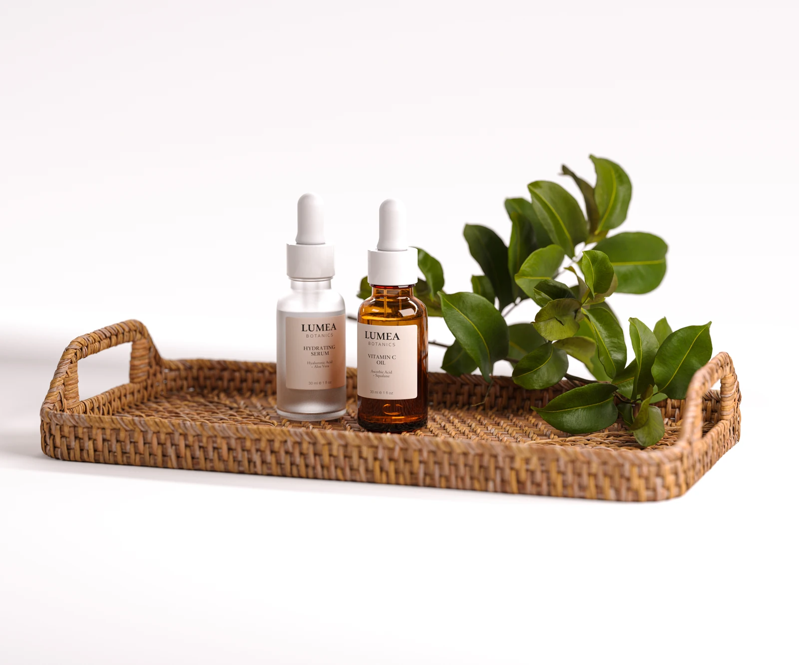 Product visualization of two dropper bottles and green leaves arranged on a woven tray